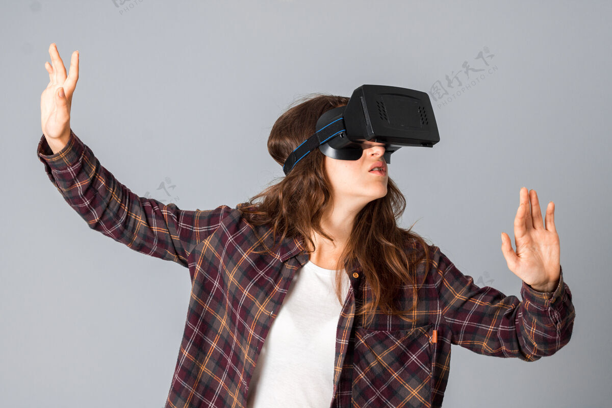 游戏在灰色墙上的工作室里 一个年轻的黑发女人正在测试一个虚拟现实头盔房子手表设备