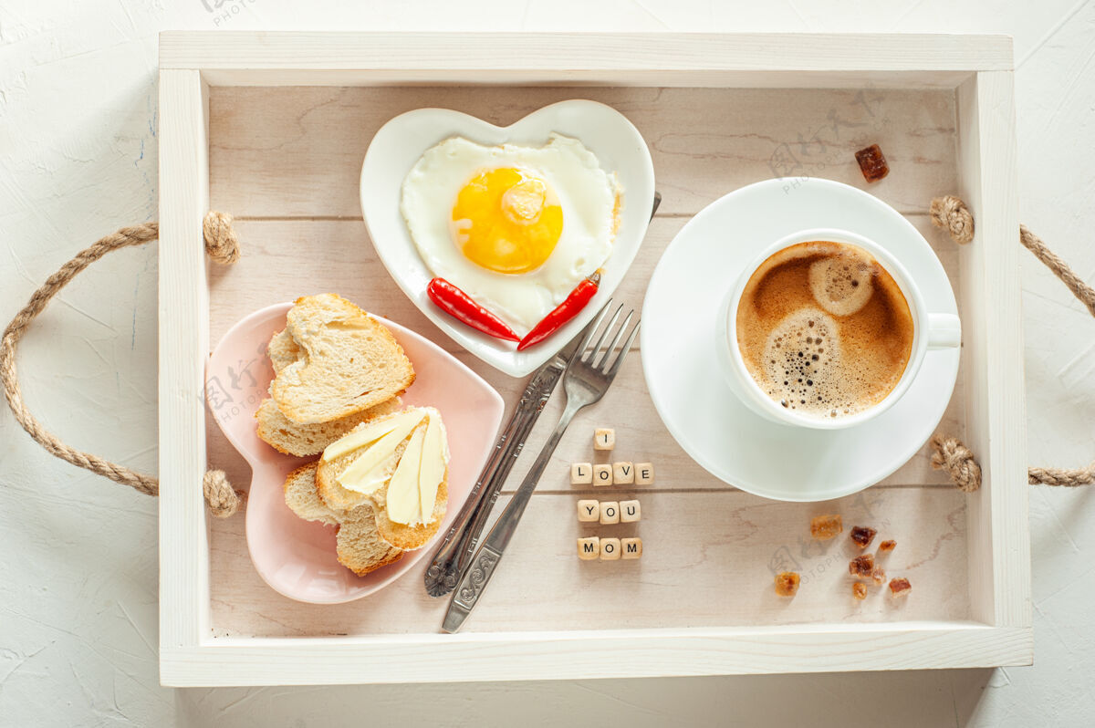 一天母亲节早餐托盘里有一杯咖啡 两盘炒蛋和心形面包 上面写着“我爱你妈妈”的字样 从上面看杯子爱问候