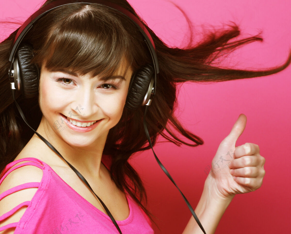 干净美丽的女人带着耳机 她正在听粉色空间上空的音乐性感优雅健康
