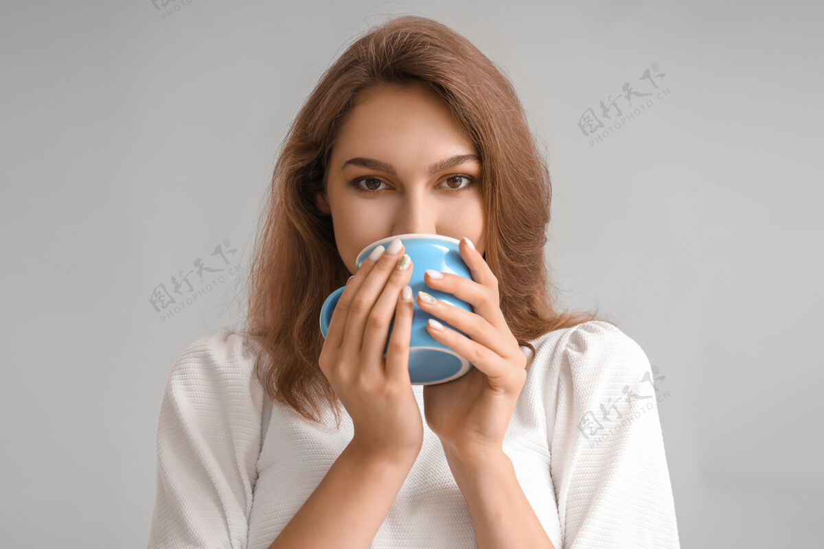 休闲美丽的年轻女子 在灰色的茶杯上芳香排毒茶点时间