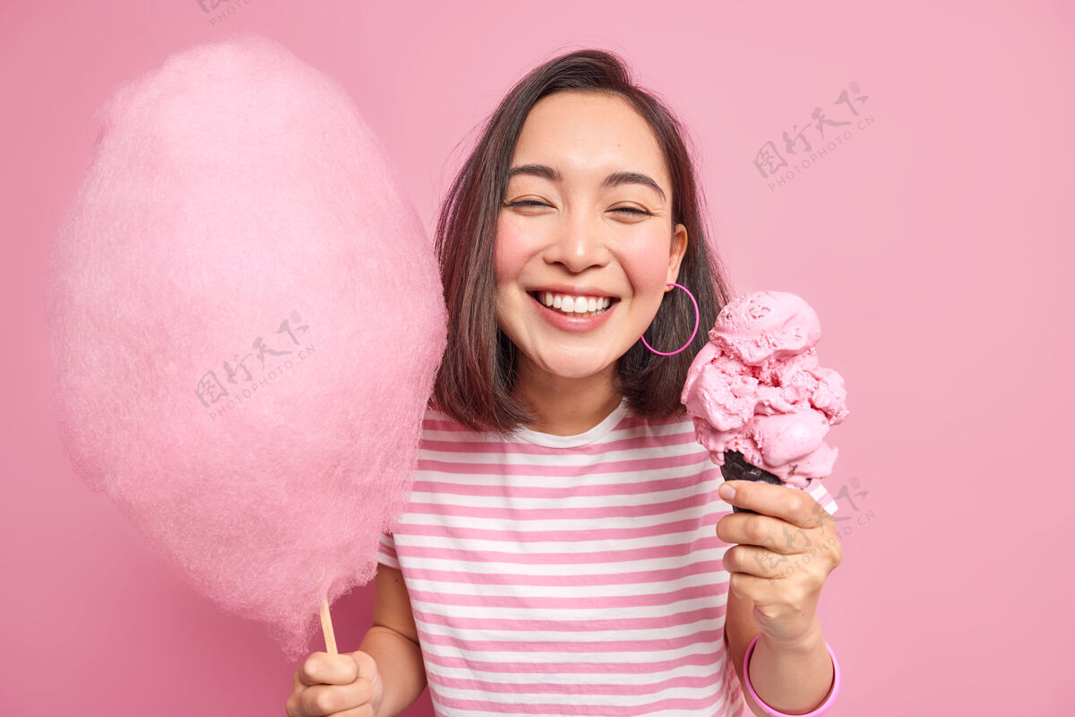 女性积极的少女有着牙齿般的微笑甜食无法想象没有美味的甜食她的生活拿着糖果牙线和冰激凌提升心情吃美味的甜点隔离在粉红色的墙上人室内牙齿
