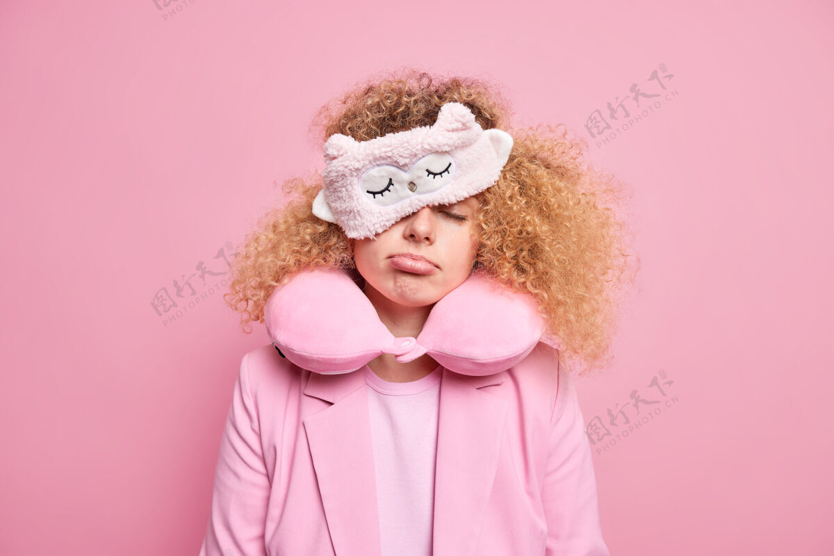枕头疲惫的女人在长途旅行后感到筋疲力尽 在旅途中试着小睡一会儿 睡意朦胧的表情戴着睡眠面罩 脖子上戴着旅行枕头 穿着正式隔离在粉红色的墙上穿模特疲劳
