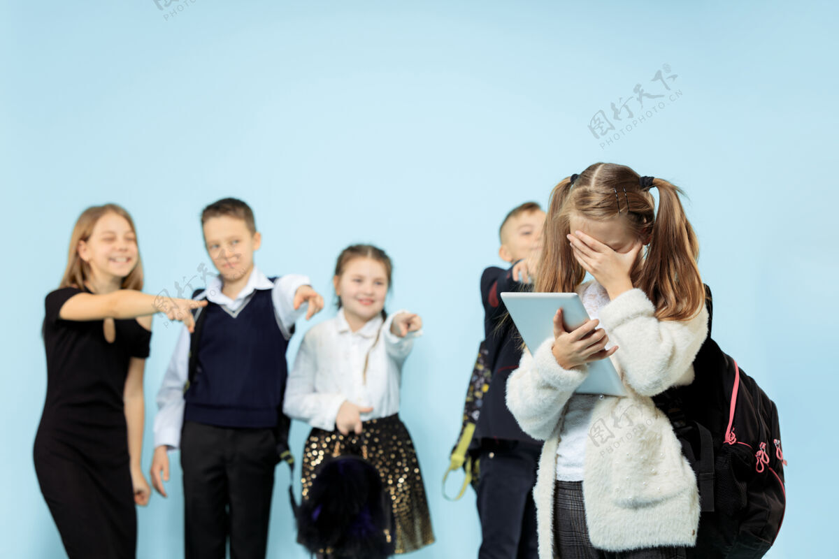 男孩小女孩独自一人站着 在孩子们嘲笑的时候遭受欺凌悲伤的小女孩坐在蓝色背景下的演播室里意识犯罪学校
