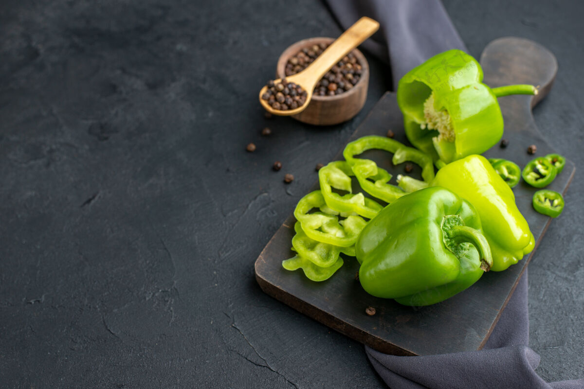健康在黑色表面上的深色毛巾上的木制砧板上切下的整个切好的青椒的正面图胡椒整个甜椒