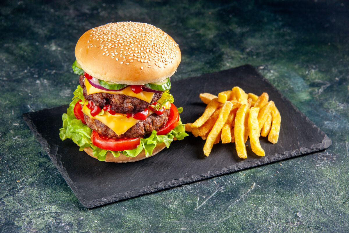 奶酪在黑色表面的深色托盘上近距离观看美味的三明治和薯条托盘快餐芝士汉堡