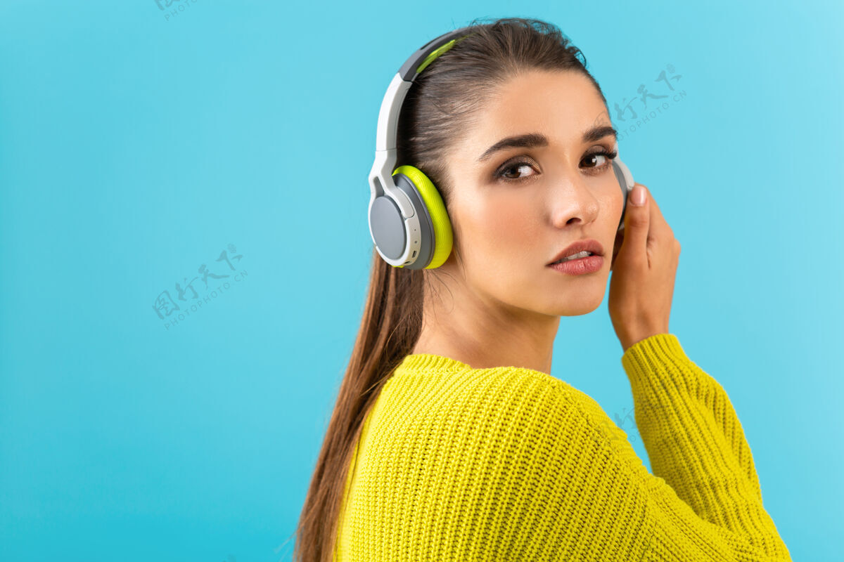 时尚迷人时尚的年轻女子戴着无线耳机听音乐快乐地穿着黄色针织毛衣五颜六色的时尚造型摆姿势欢乐音频耳机