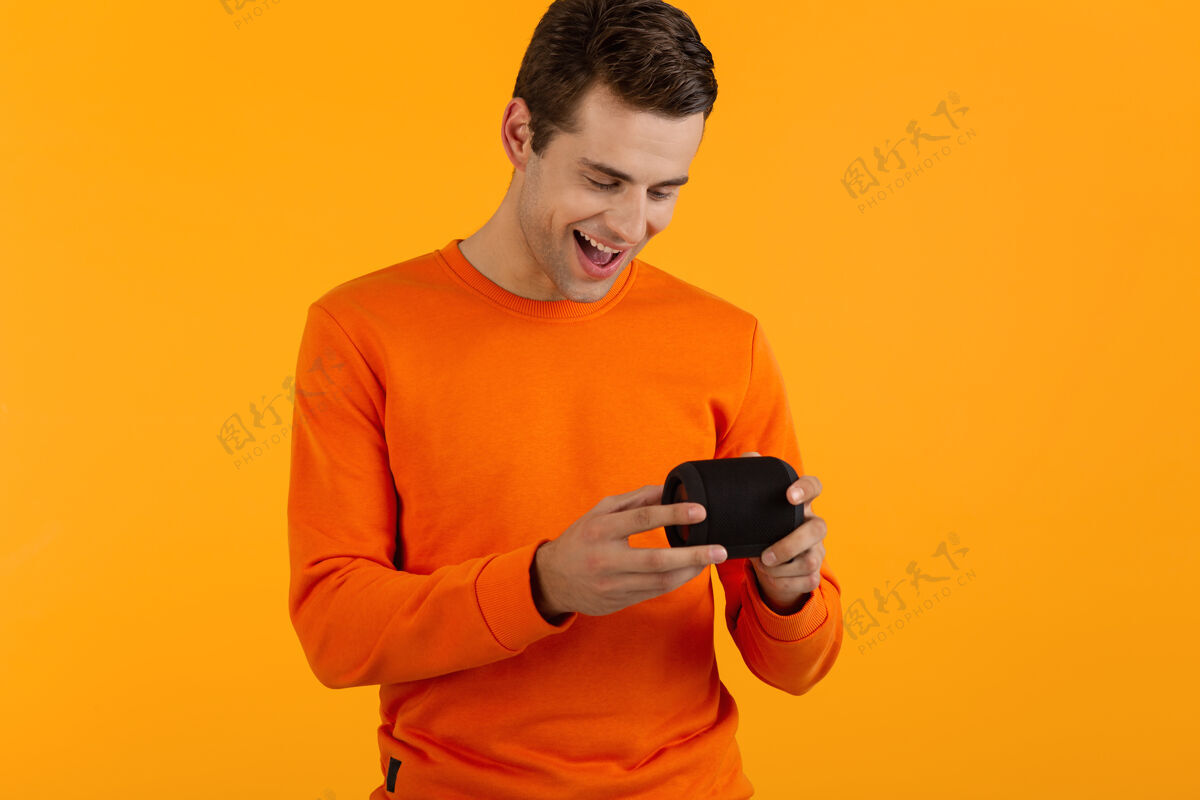 娱乐时尚微笑的年轻人穿着橙色毛衣手持无线扬声器快乐地听音乐玩得开心情感城市姿势