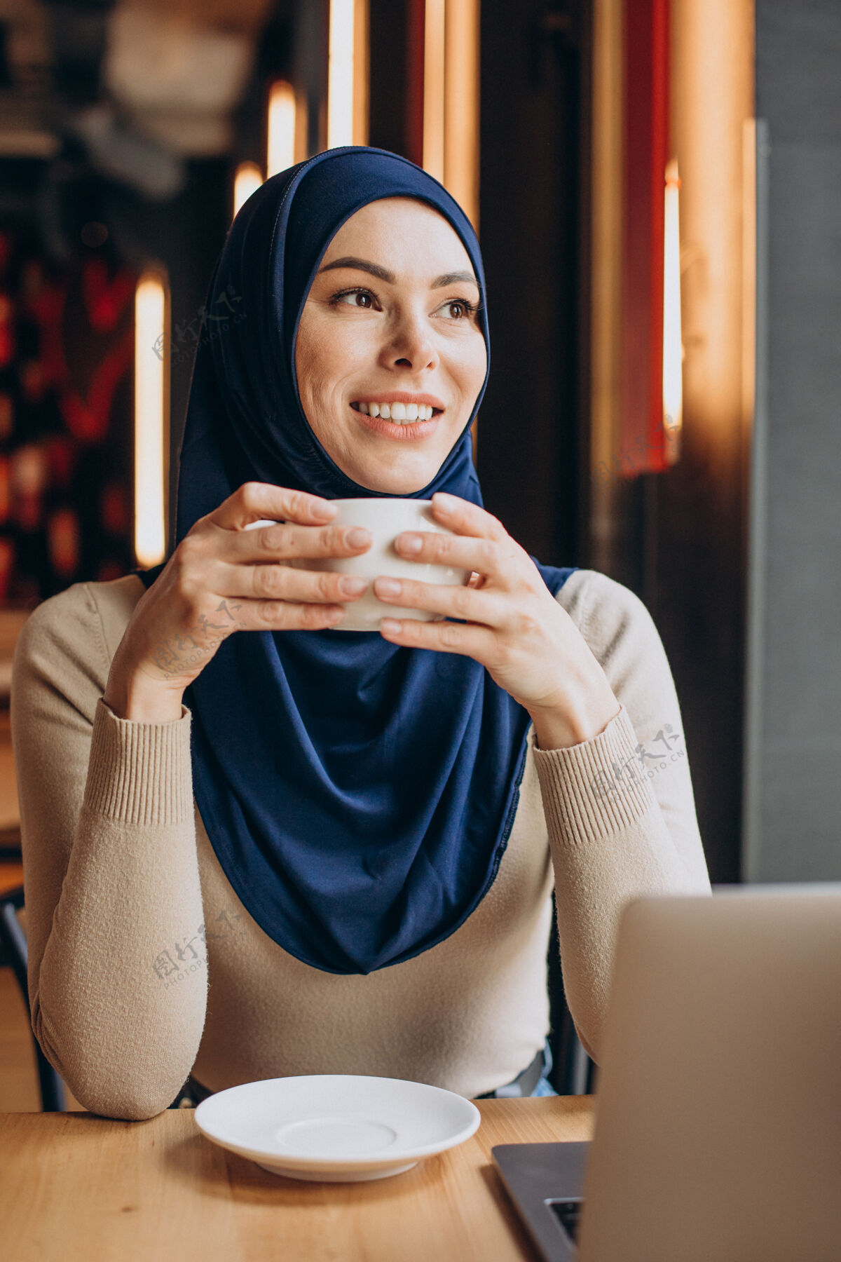 穆斯林现代穆斯林妇女在咖啡馆里喝茶和操作电脑在线工作笔记本电脑穆斯林妇女