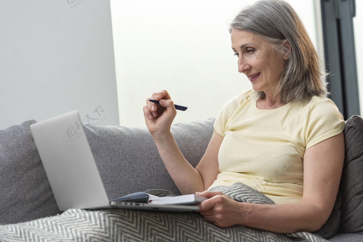 老年人家里的老太太在沙发上用笔记本电脑记笔记室内老年人成人