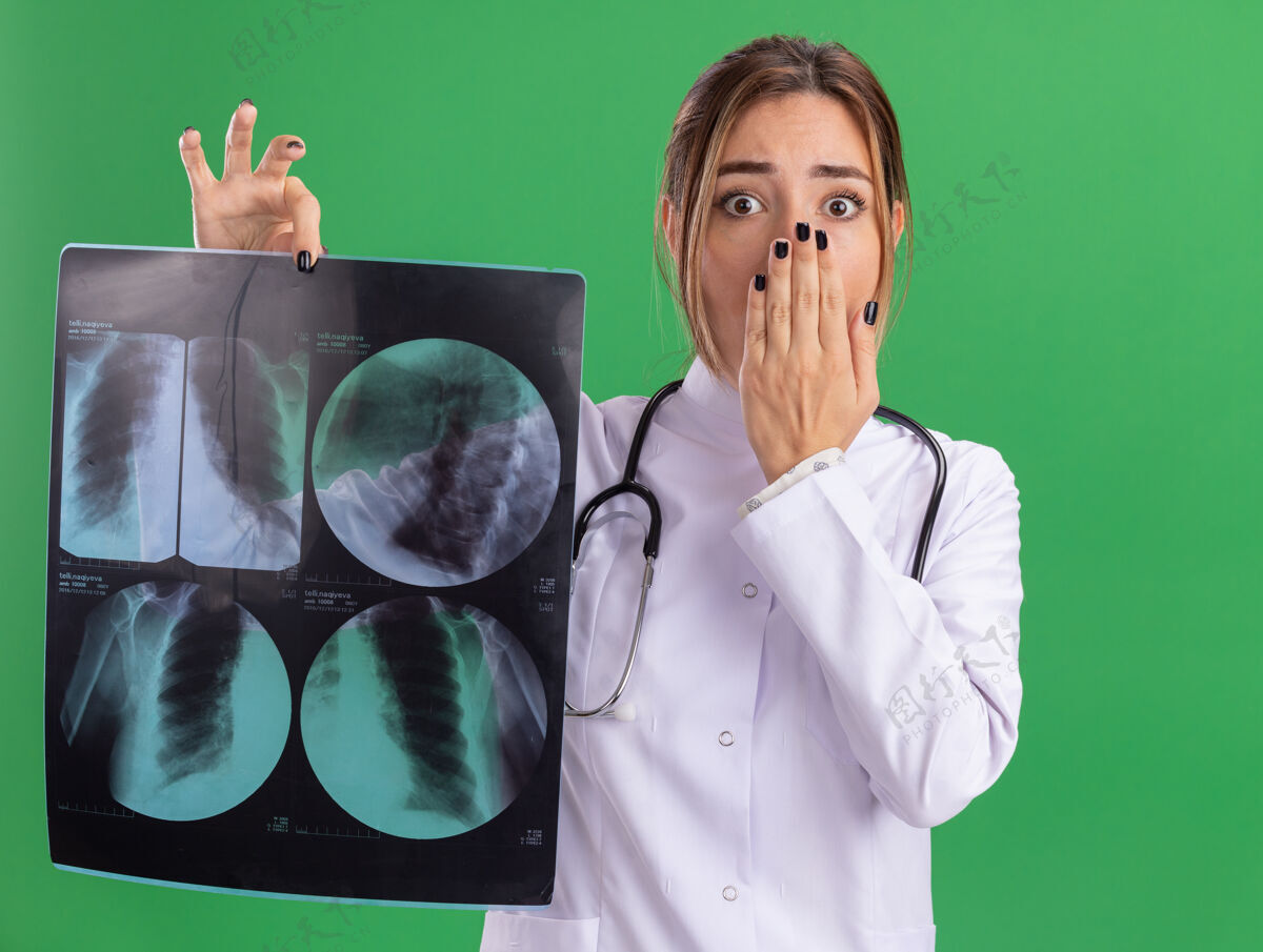 年轻年轻的女医生被吓坏了 穿着医用长袍 听诊器拿着x光片 手捂着嘴 隔离在绿色的墙上人手掩护