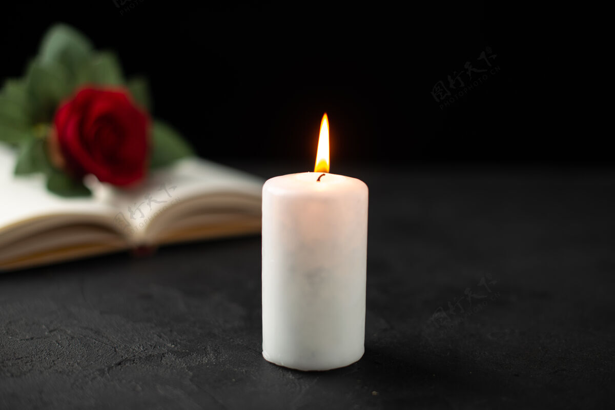 烛光打开的书和蜡烛上的黑玫瑰的正面视图葬礼火红玫瑰