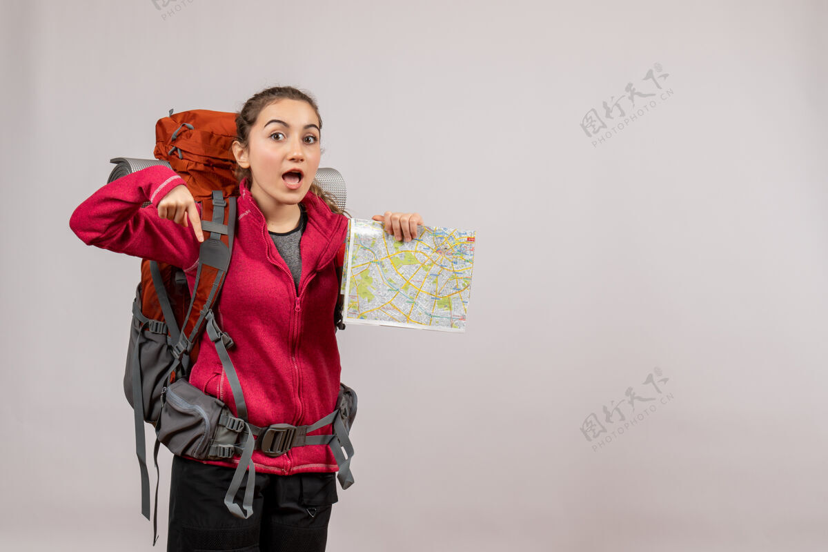 旅游正面图年轻的旅行者拿着大背包拿着地图指着地板旅行者旅游灰色