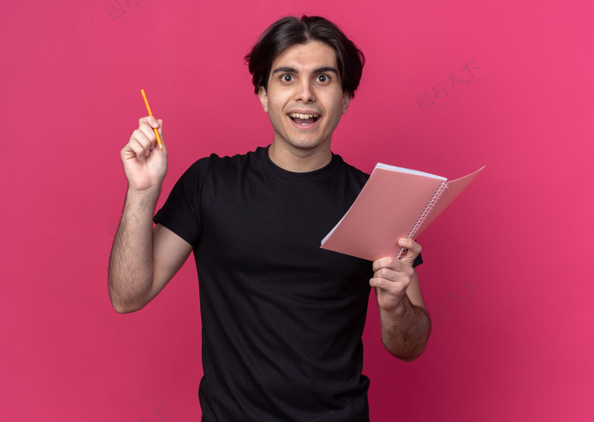 男人印象深刻的年轻帅哥穿着黑色t恤拿着铅笔笔记本-隔离在粉红色的墙上年轻印象人
