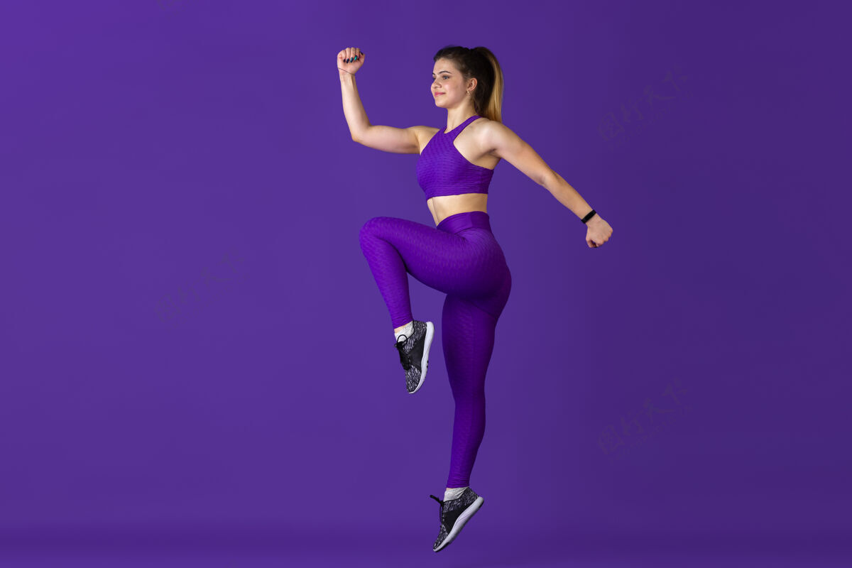 紧缩在跳跃年轻漂亮的女运动员在练习 单色紫色肖像运动型白种人适合模型训练健美 健康的生活方式 美丽和行动的概念人举重运动