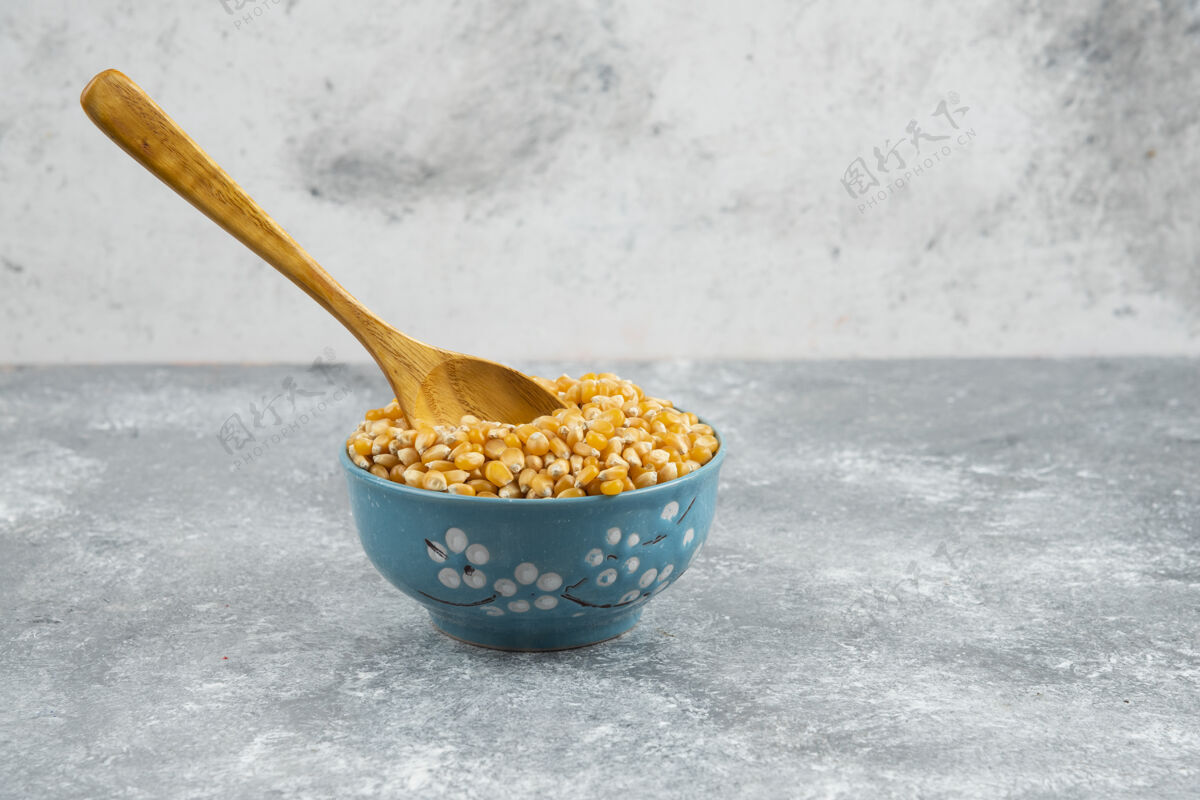 勺子用勺子把生玉米粒放在蓝碗里种子内核谷类