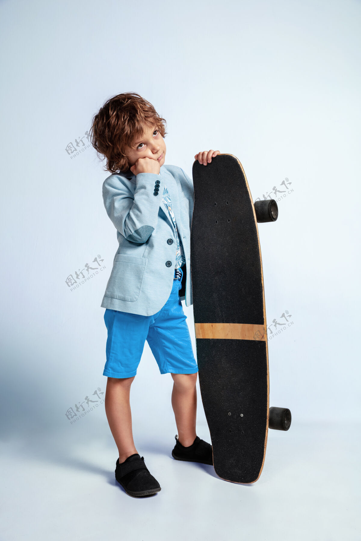 滑板在白色的墙上 穿着休闲服 在滑板上滑冰的小男孩骑着 看起来很快乐白人男性学龄前儿童 有着明亮的面部表情童年 表情 快乐极端表情年轻
