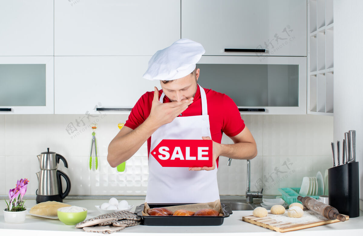 厨房在白色厨房里 年轻昏昏欲睡的男厨师展示销售标志的俯视图职业工作顶部