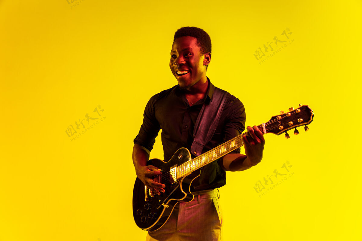 蓝调年轻的非洲裔美国音乐家在霓虹灯下像摇滚明星一样在黄色背景下弹吉他音乐概念 爱好 节日 露天快乐的家伙即兴表演 唱歌娱乐衬衫立场