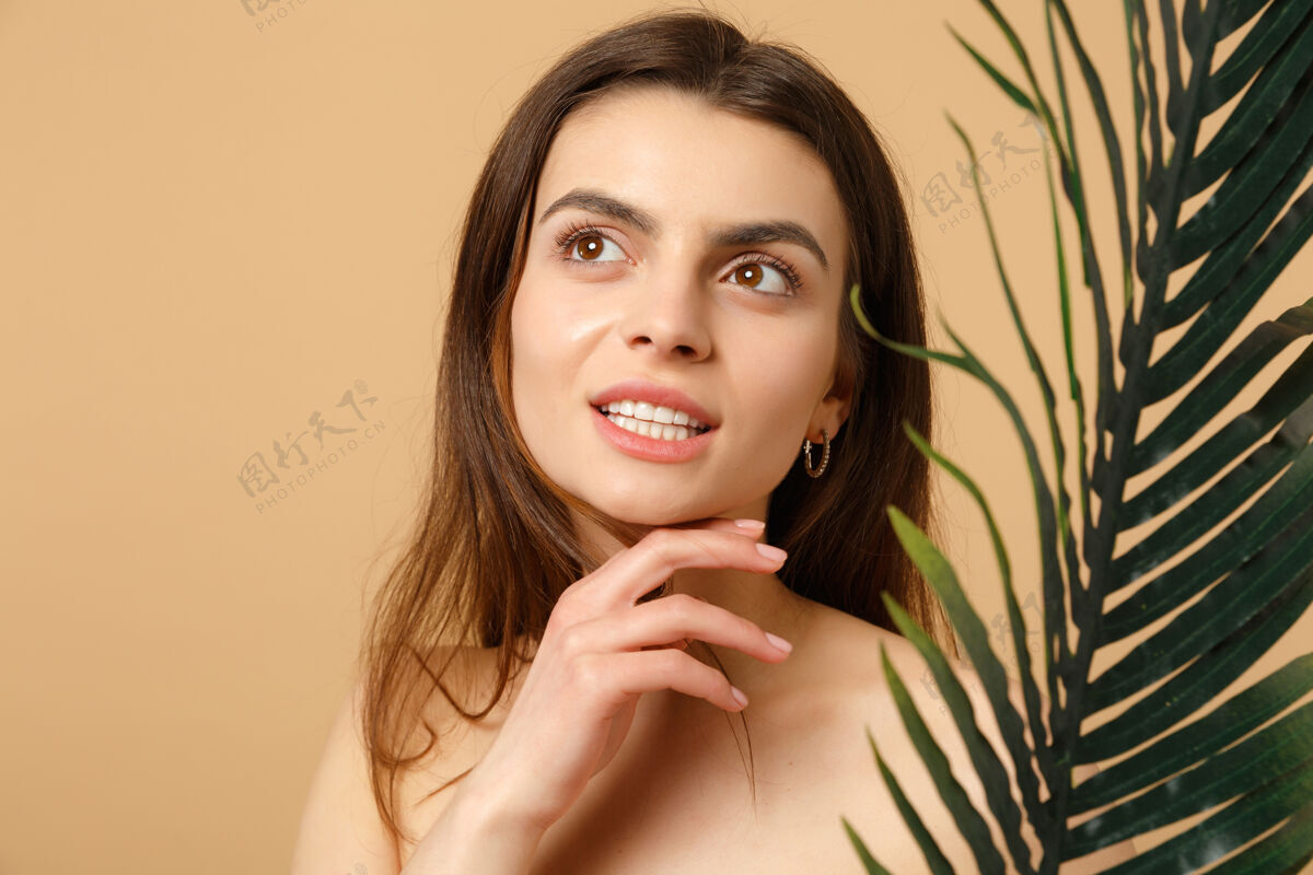 美丽特写黑发半裸女人完美的皮肤 裸妆和棕榈叶隔离在米色粉彩墙上女人清晰叶