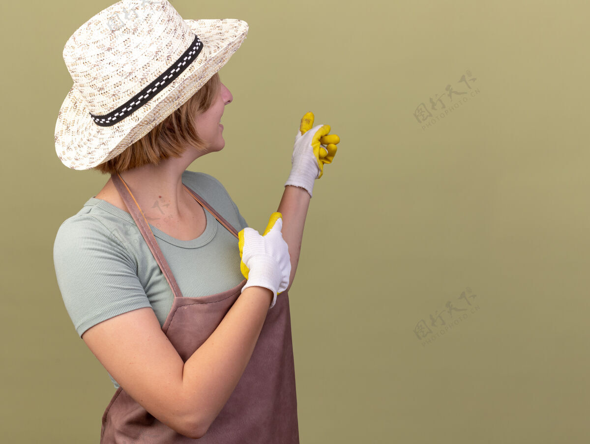 指点微笑着的年轻斯拉夫女园丁戴着园艺帽和手套 看着并指着后面穿花园帽子