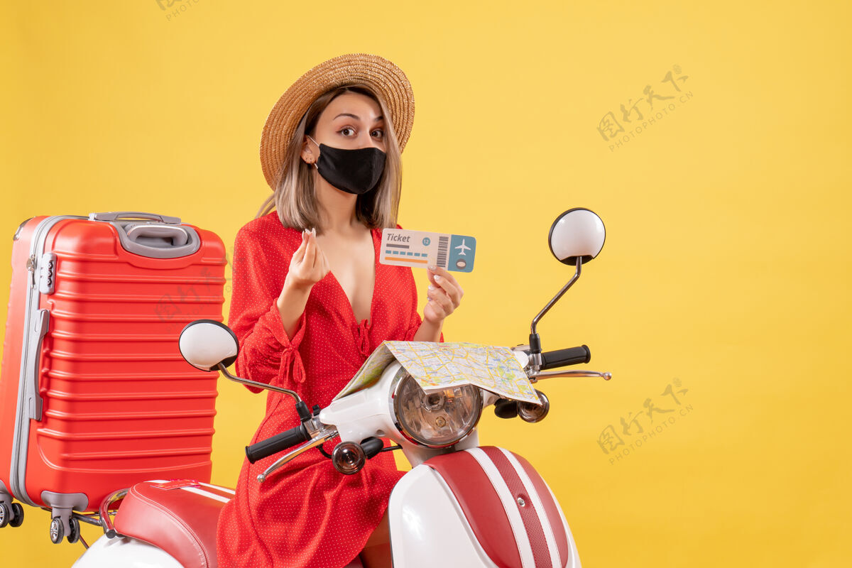 持有正面图：戴着黑色面罩的年轻女士手持“售票赚钱”的牌子轻便摩托车车辆度假