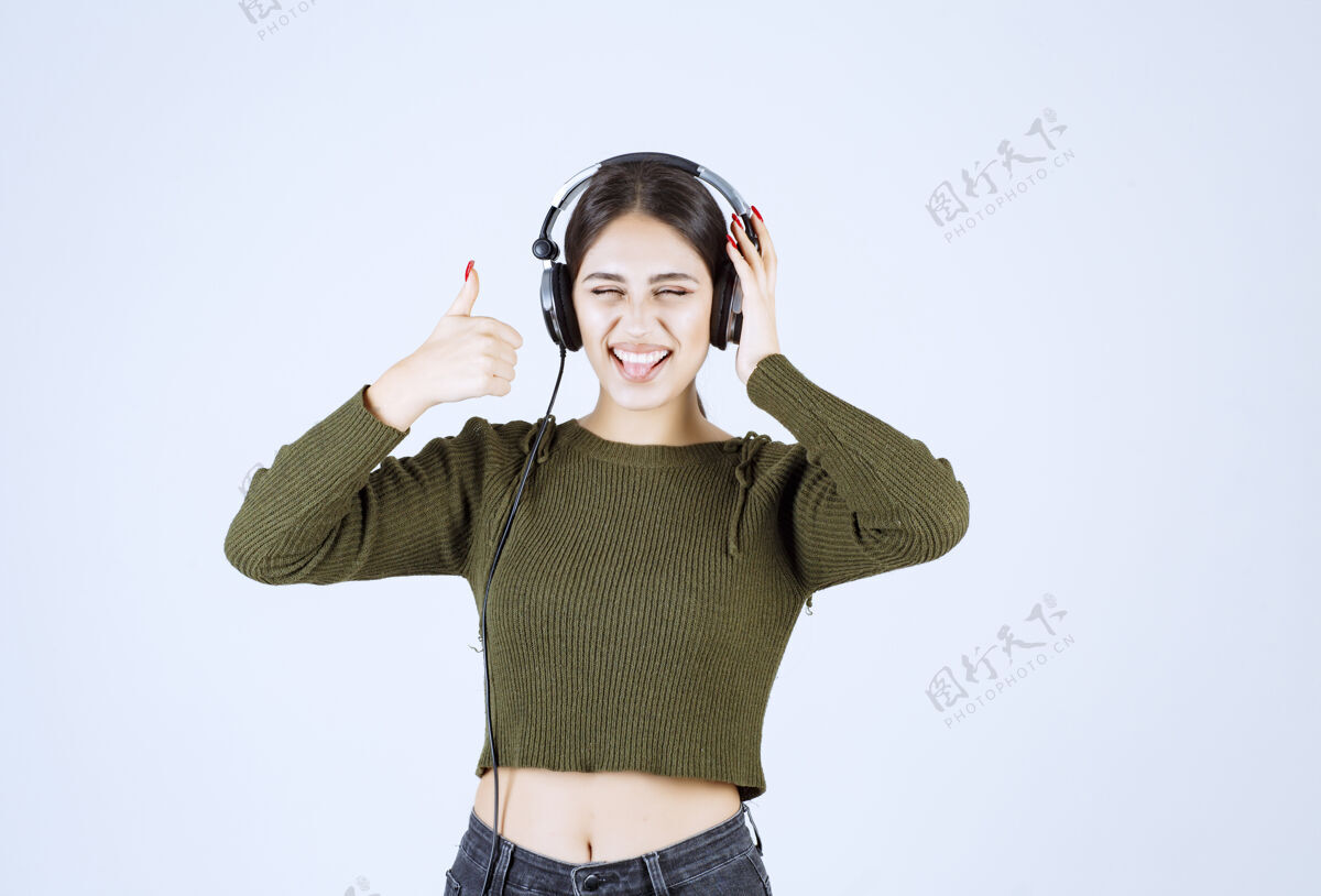 女人戴着耳机听音乐竖起大拇指的年轻女孩的画像情感女士模特