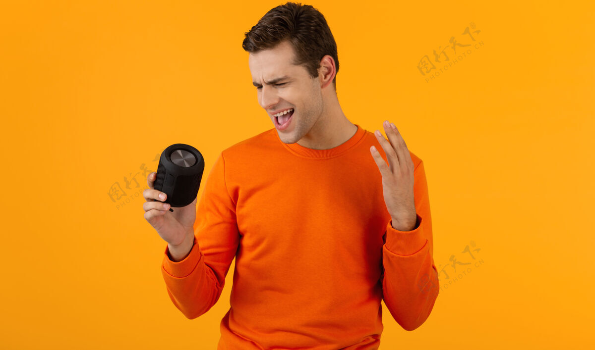 城市时尚微笑的年轻人穿着橙色毛衣手持无线扬声器快乐地听音乐玩得开心搞笑时髦积极