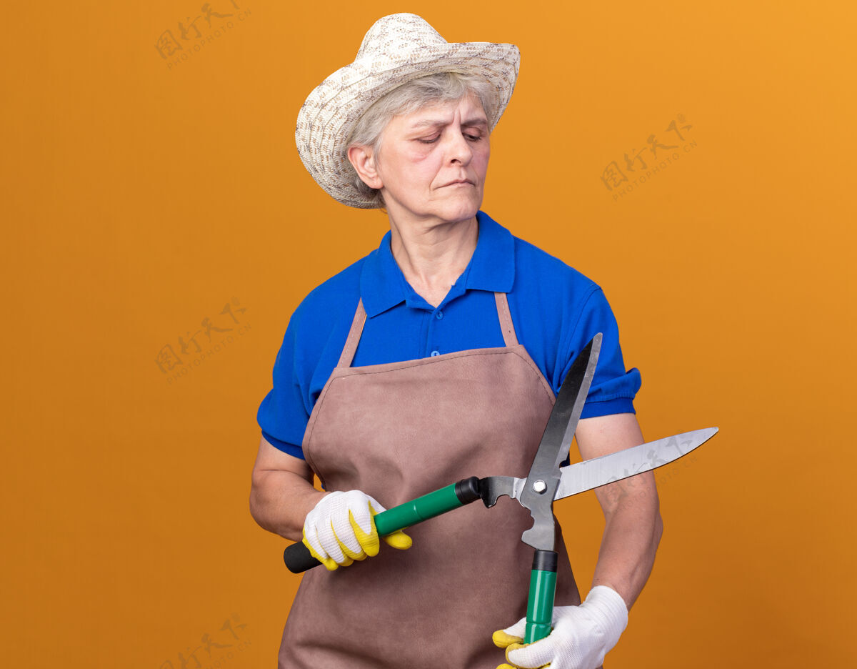 女自信的上了年纪的女园丁戴着园艺帽和手套拿着园艺剪刀看着帽子手套自信