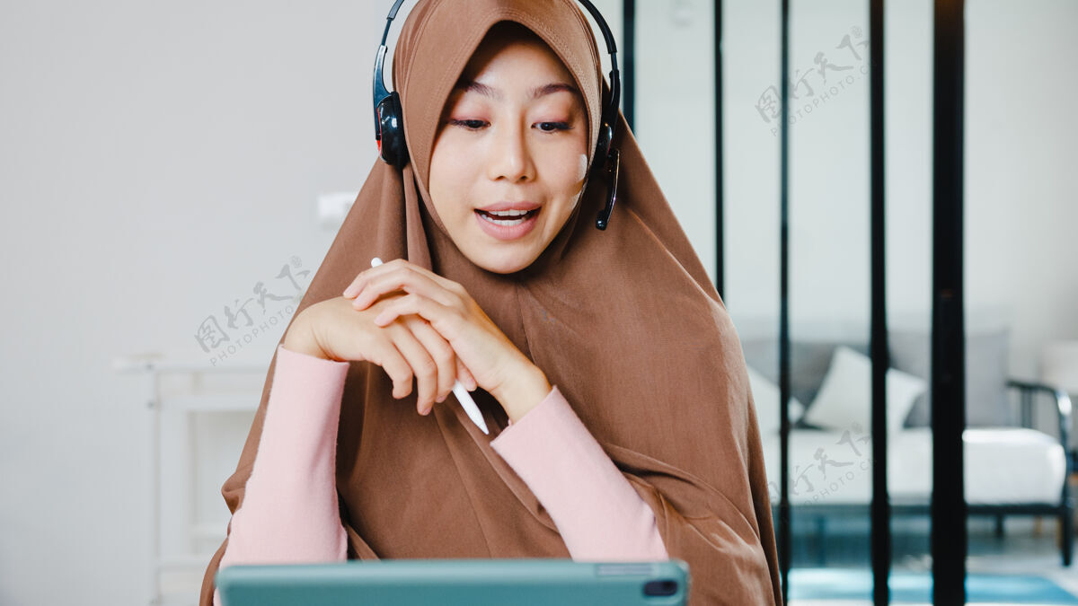 商务穆斯林女士戴着耳机使用数字平板电脑在家里厨房工作时 通过视频会议与同事谈论销售报告厨房女性房子