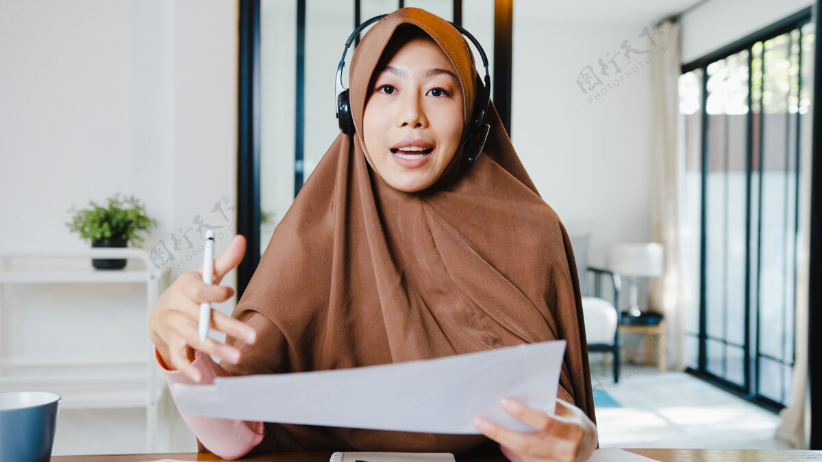 社交穆斯林女士戴着耳机 用笔记本电脑和同事通过视频电话谈论销售报告 同时在客厅远程工作工作穆斯林女性