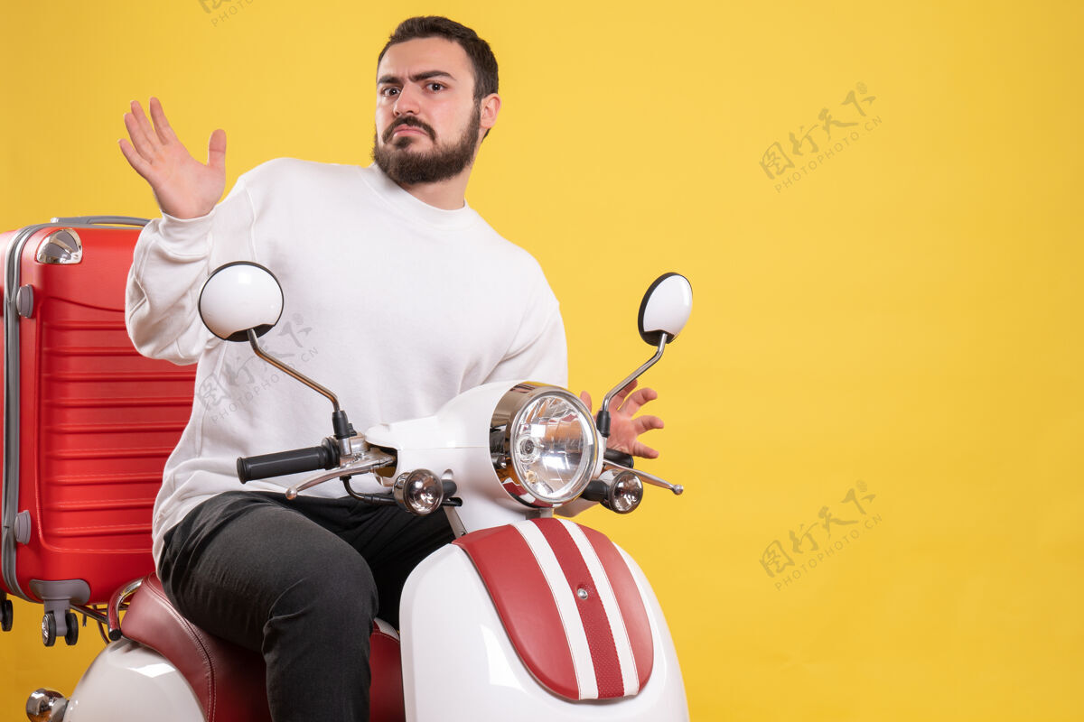 车辆在孤立的黄色背景上 困惑的年轻人坐在摩托车上 手提箱在上面年轻人训练手提箱