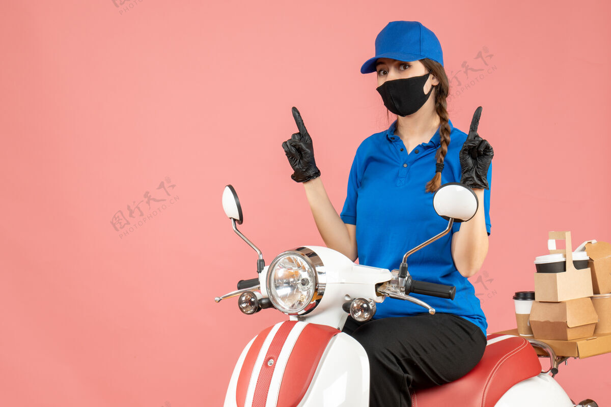 医疗俯视图上的女快递员戴着医用口罩和手套坐在滑板车上 在粉彩桃色背景上向上传递订单桃车辆穿