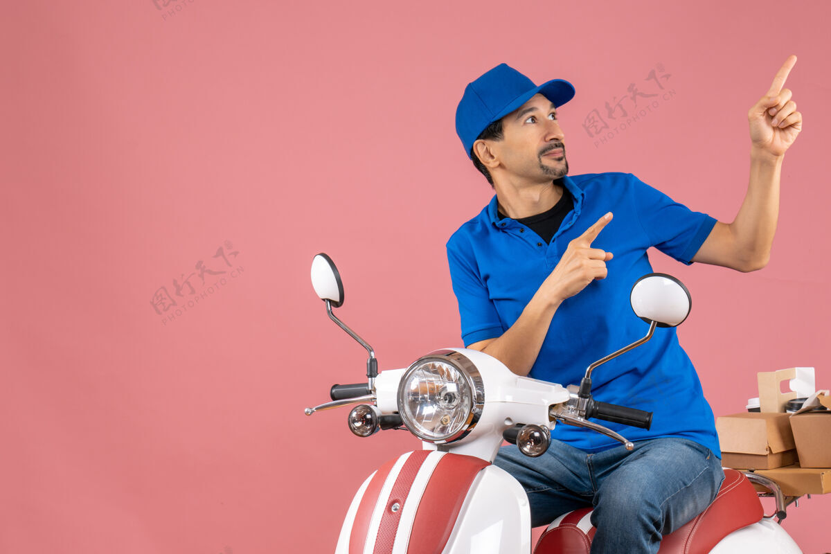 滑板车顶视图上的快递员戴着帽子坐在滑板车上传递订单 转身指向粉彩桃色背景上指着摩托车男
