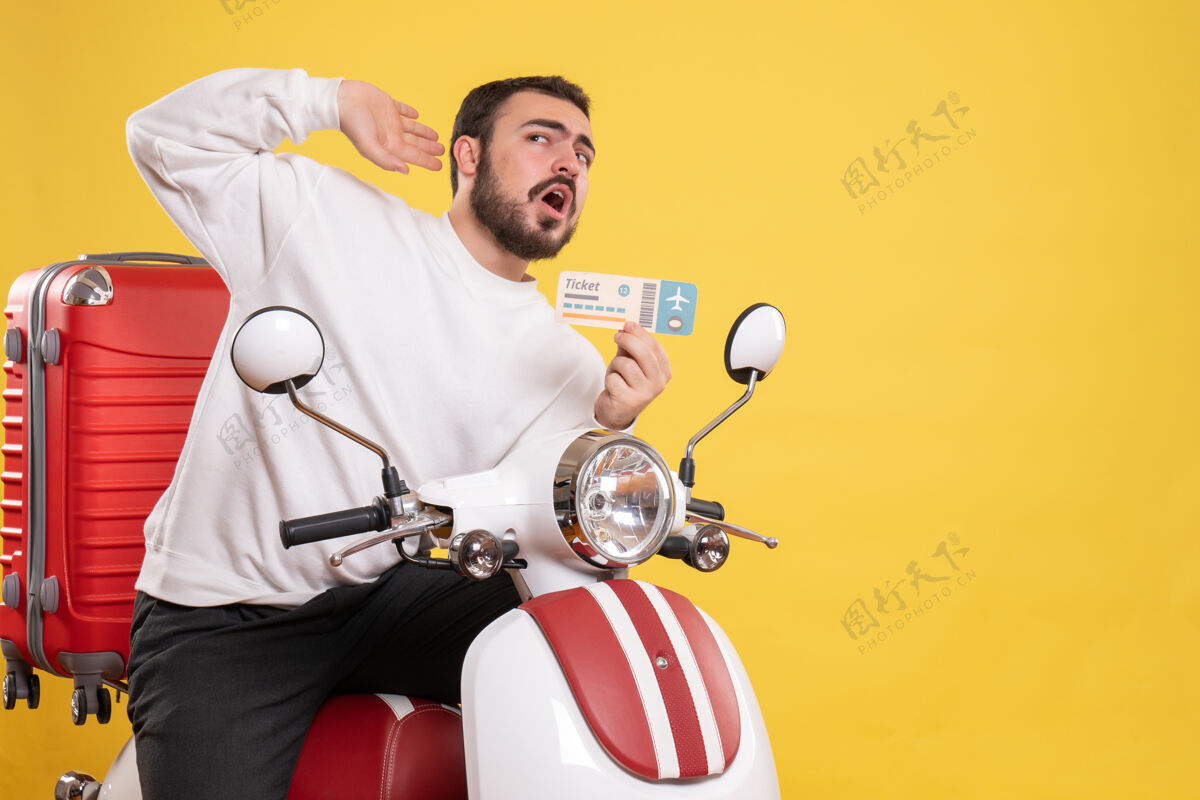 背景前视图：年轻的旅行男子坐在摩托车上 提着手提箱 拿着车票 在孤立的黄色背景上听着最后的闲话前面票摩托车