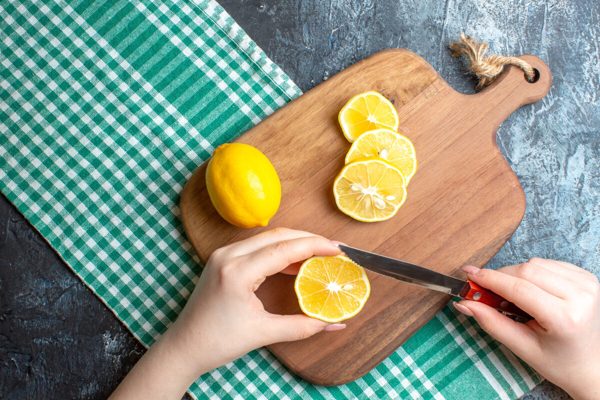 可食用水果在黑暗背景下 一只手在木制砧板上切碎新鲜柠檬的俯视图新鲜健康柑橘