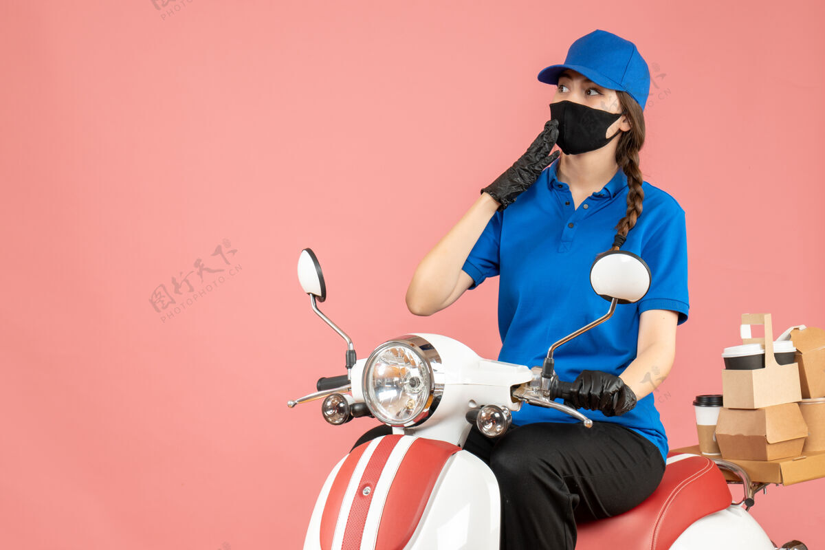 思考前视图思考快递女孩戴着医用面罩和手套坐在滑板车上传递粉彩桃背景的命令人粉彩桃