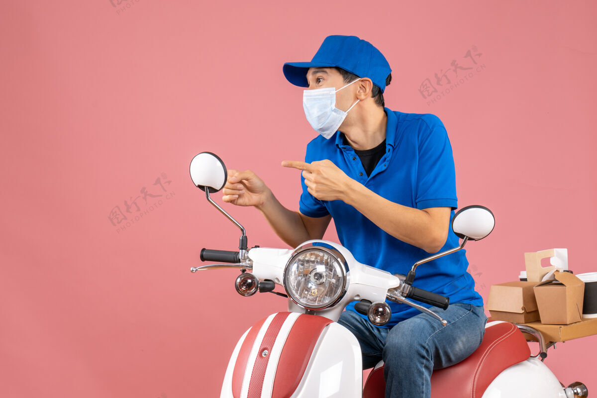坐前视图集中快递员戴着医疗面具戴着帽子坐在粉彩桃色背景的踏板车上桃运动穿
