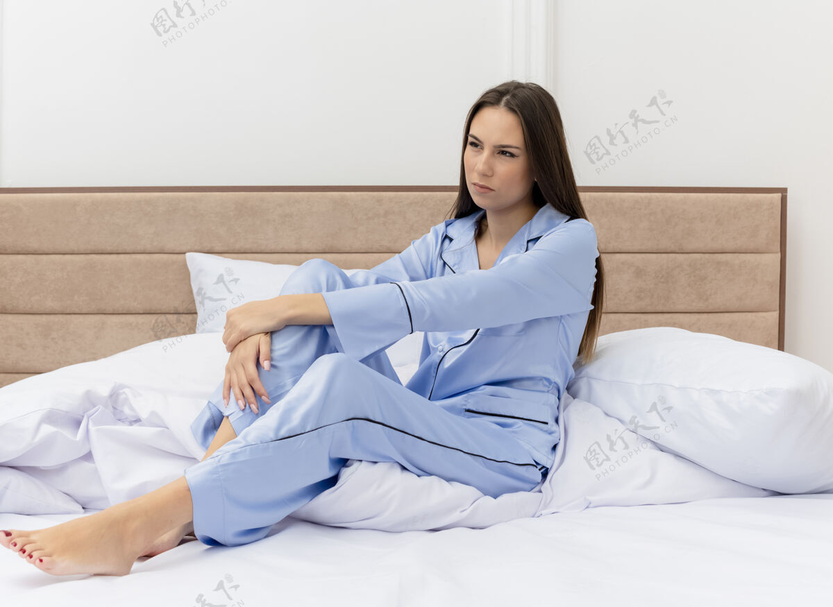 卧室穿着蓝色睡衣的年轻漂亮女人坐在床上 严肃地看着卧室内部灯光严肃室内