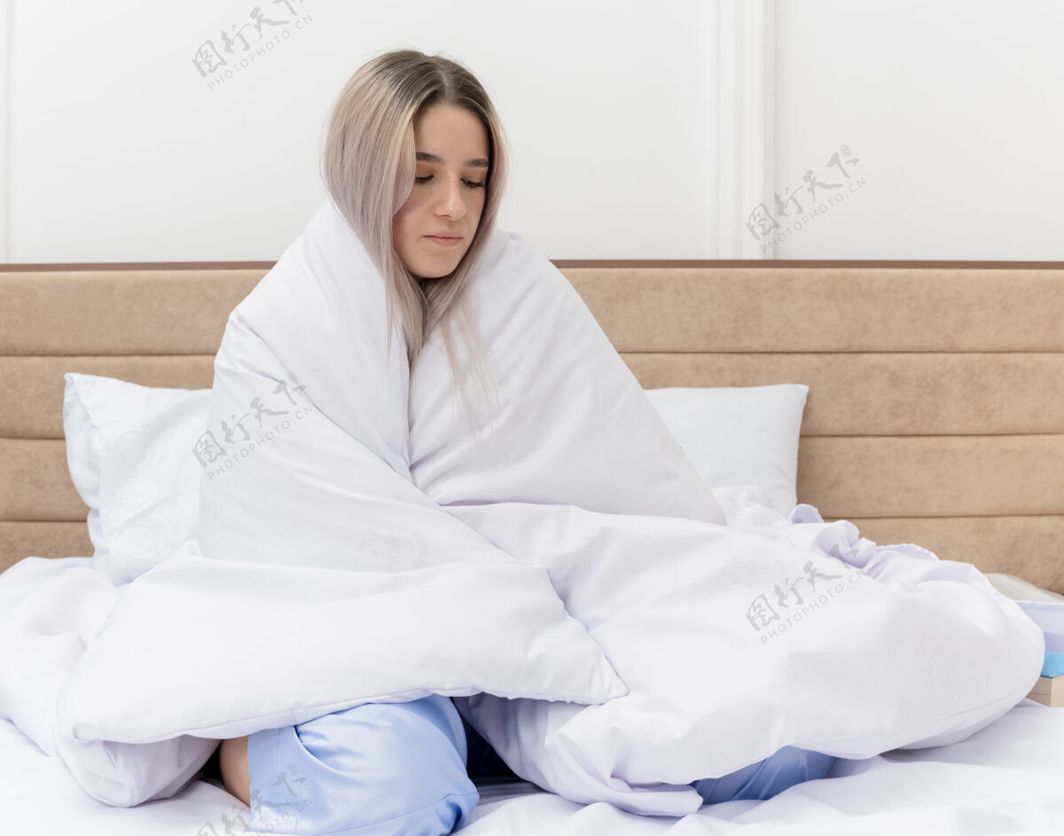 女人穿着蓝色睡衣的年轻美女坐在床上 裹着毯子 卧室里感觉不舒服室内蓝色漂亮