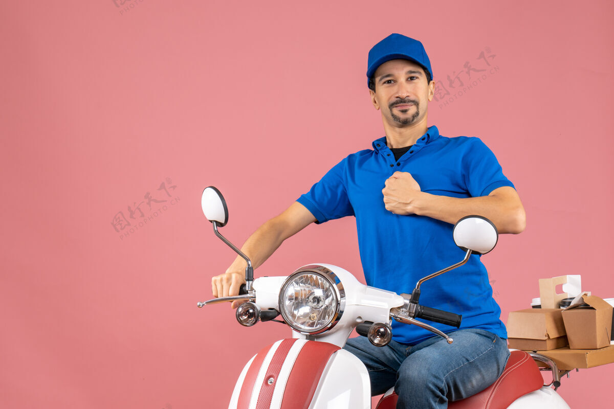 肌肉胸怀大志的快递员戴着帽子坐在滑板车上 展现他肌肉发达的粉色背景游戏设备桃摩托车