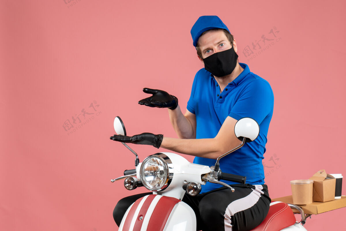 运动正面图身着蓝色制服 戴着粉色病毒面罩的男快递员自行车上的工作快递快餐covid服务工作视图人工作