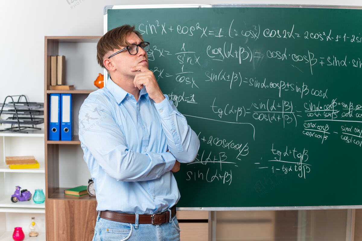 数学戴着眼镜的年轻男老师站在教室里数学公式的黑板旁困惑地抬头看拼图教室年轻人