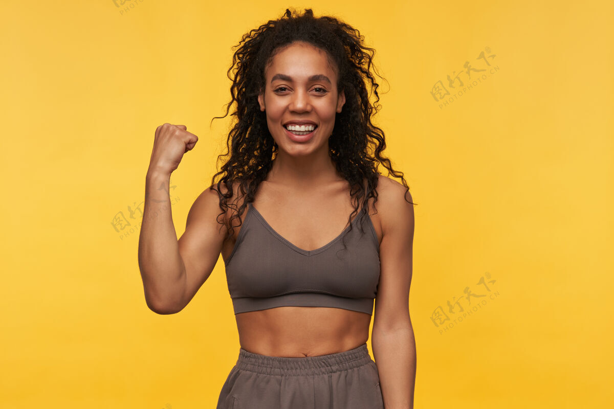 深色快乐成功的年轻健身女展示胜利姿态 庆祝成功隔离黄墙情感女士胜利