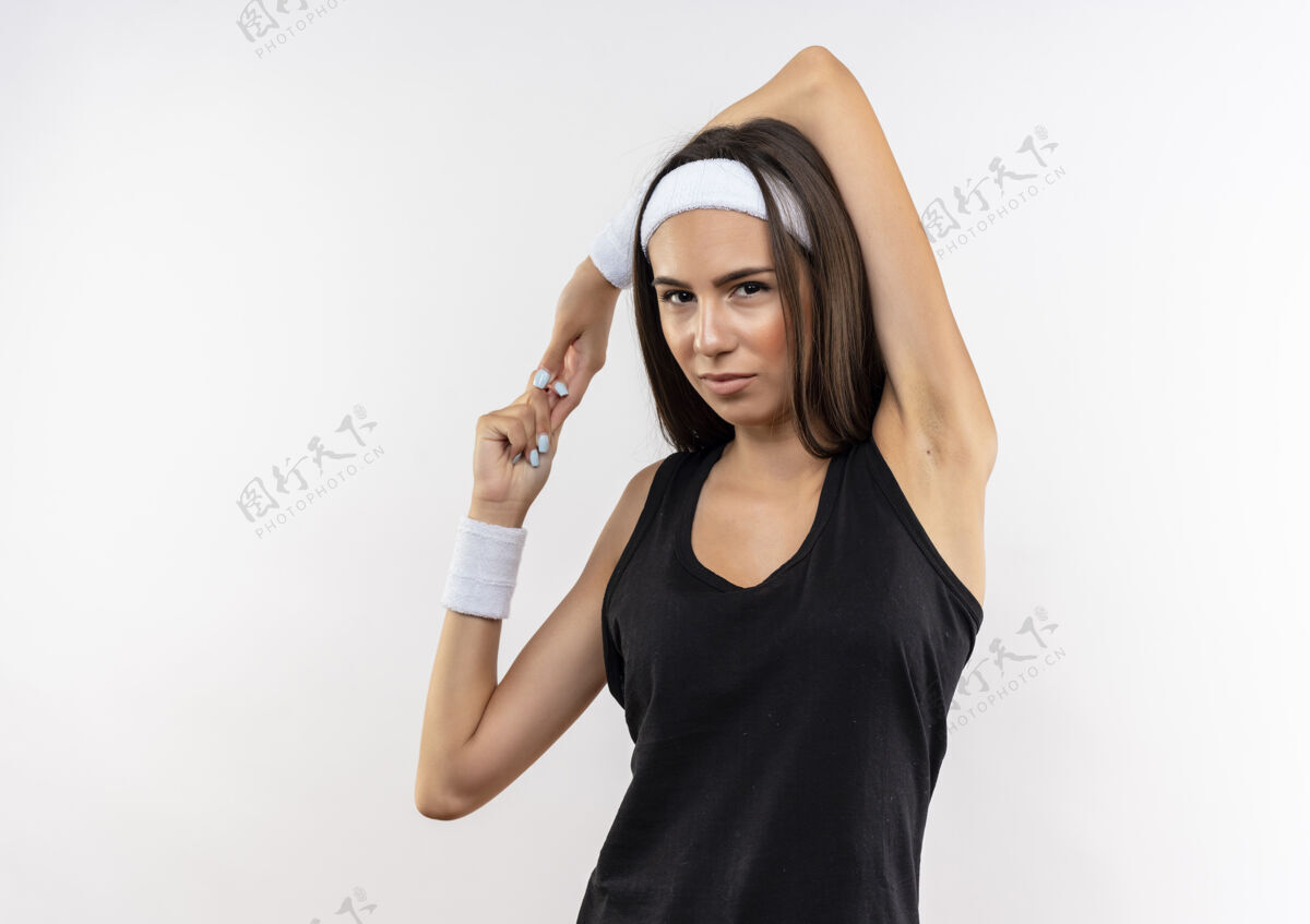 运动自信漂亮的运动女孩戴着头带和腕带把手臂放在头上 保持双手在一起 在白色的墙壁与复制空间隔离保持漂亮手