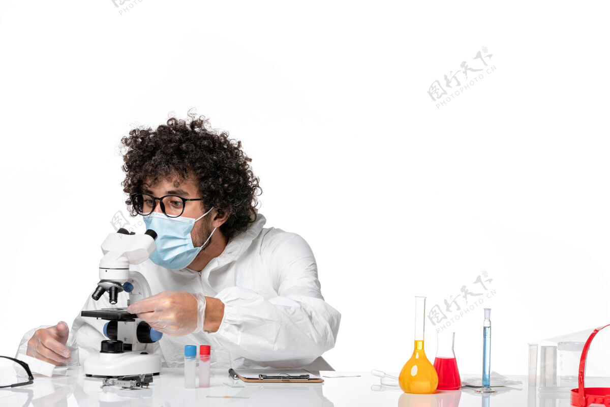 视图男医生穿着防护服 带着无菌口罩拿着样品 用显微镜对着白色成人病毒防护