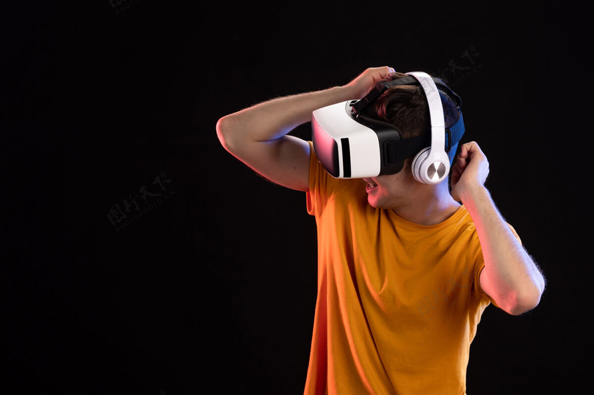年轻人年轻人戴着耳机在黑暗的墙上玩虚拟现实的画像男性人黑人