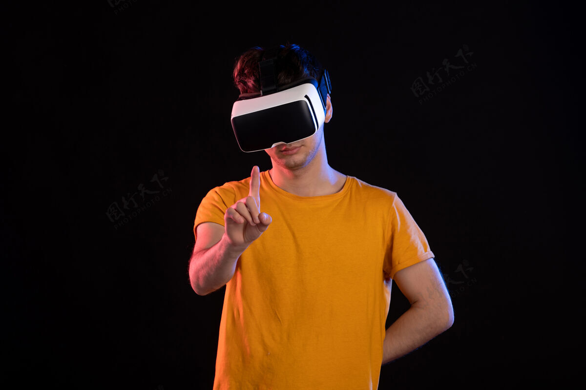 肖像在黑暗的墙壁上玩虚拟现实的年轻男性的正面视图人人护目镜