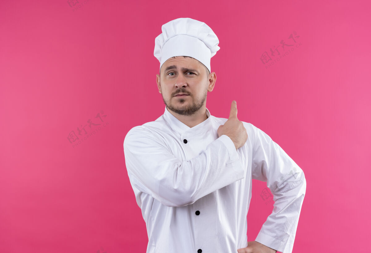 年轻自信的年轻帅哥厨师身着厨师制服指着身后孤零零的粉色墙壁厨师指点自信