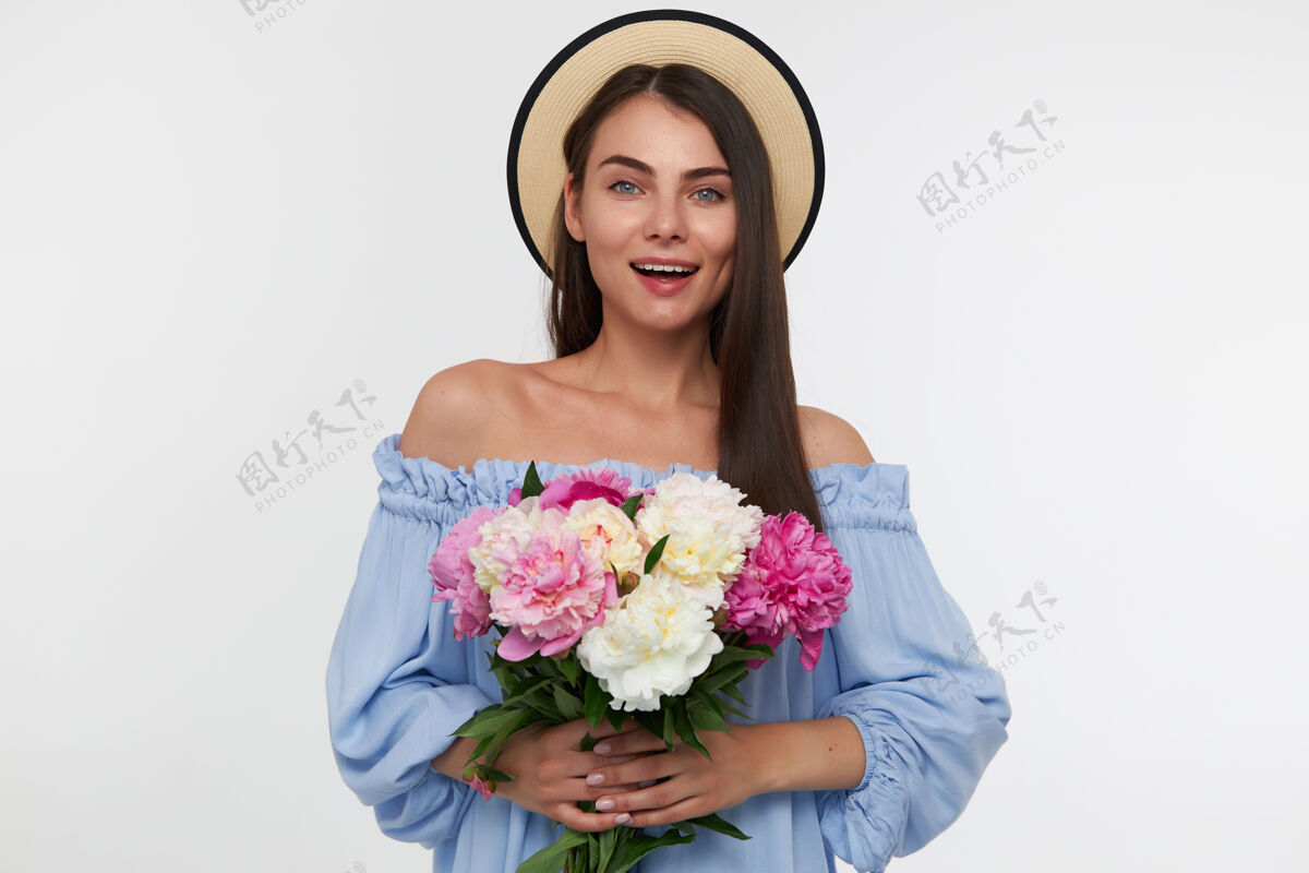 美丽一幅迷人女孩的肖像 笑容灿烂 留着深褐色的长发 戴着帽子 穿着蓝色漂亮的裙子 手里拿着一束漂亮的花拍摄室内牙齿