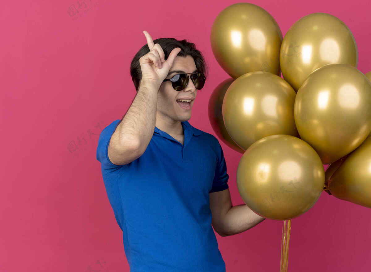 男人戴着太阳镜的快乐英俊的白种人手持氦气球和手势持有标志快乐